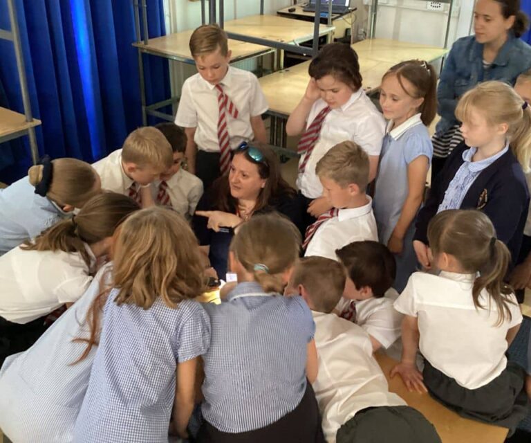 Dr Fay Couceiro looking through a microscope surrounded by a group of children