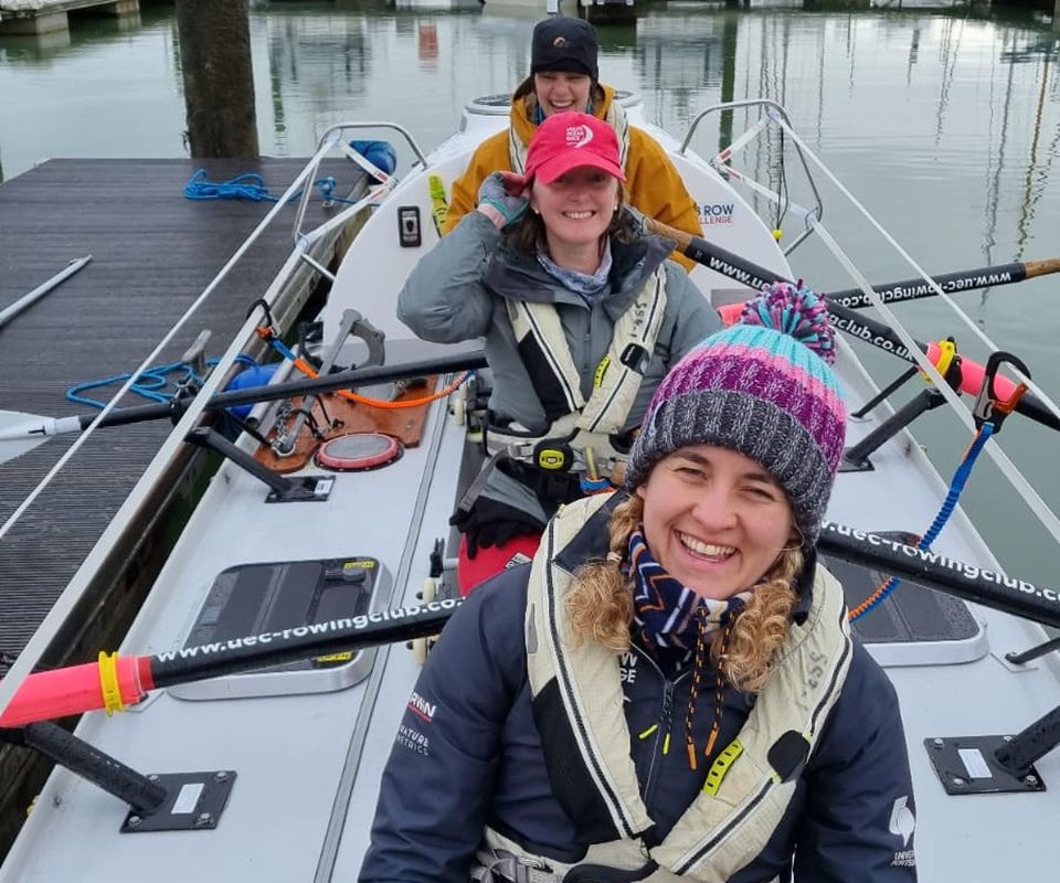 Three women on a rowing boat in a harbour before they set off on a training row